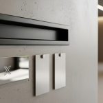Buzón negro minimalista con placa metalizada y logo X en pared
