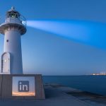 Faro moderno blanco con logo LinkedIn en un muelle al atardecer