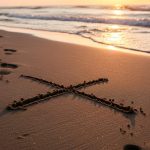Huellas en arena alejándose de una gran X en playa