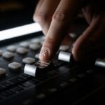 mano de ingeniero ajustando fader en consola profesional con logo de X pintada en el dedo