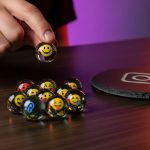 Mano lanza canica con emoji sonriente sobre mesa de madera