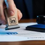 Mano sosteniendo sello de goma con logo LinkedIn sobre documento