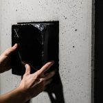 Manos ajustando bloque de obsidiana con logo X en pared concreta