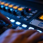 Manos ajustando los controles deslizantes de una consola de audio con el logotipo de LinkedIn grabado en relieve