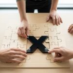 Manos colaborando para completar rompecabezas con pieza negra brillante en forma de X