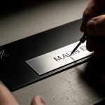Manos modificando placa metálica negra con herramienta de grabado.
