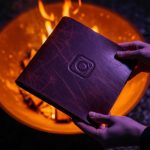 Manos sosteniendo álbum de cuero junto a hoguera nocturna