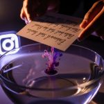 Manos sumergiendo papel en agua con tinta disolviéndose logo Instagram