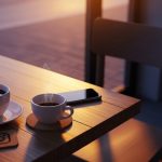 Mesa de cafetería con smartphone y tazas de café humeante con posa vaso de instagram