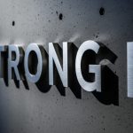 Muro de hormigón oscuro con palabra STRONG en metálico tridimensional destacado y logo de LinkedIn
