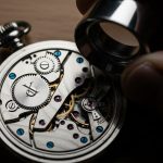 Relojero con lupa examinando reloj de bolsillo intrincado en banco
