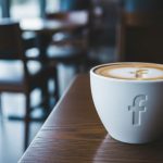 Taza café blanca con logo Facebook sobre mesa madera oscura