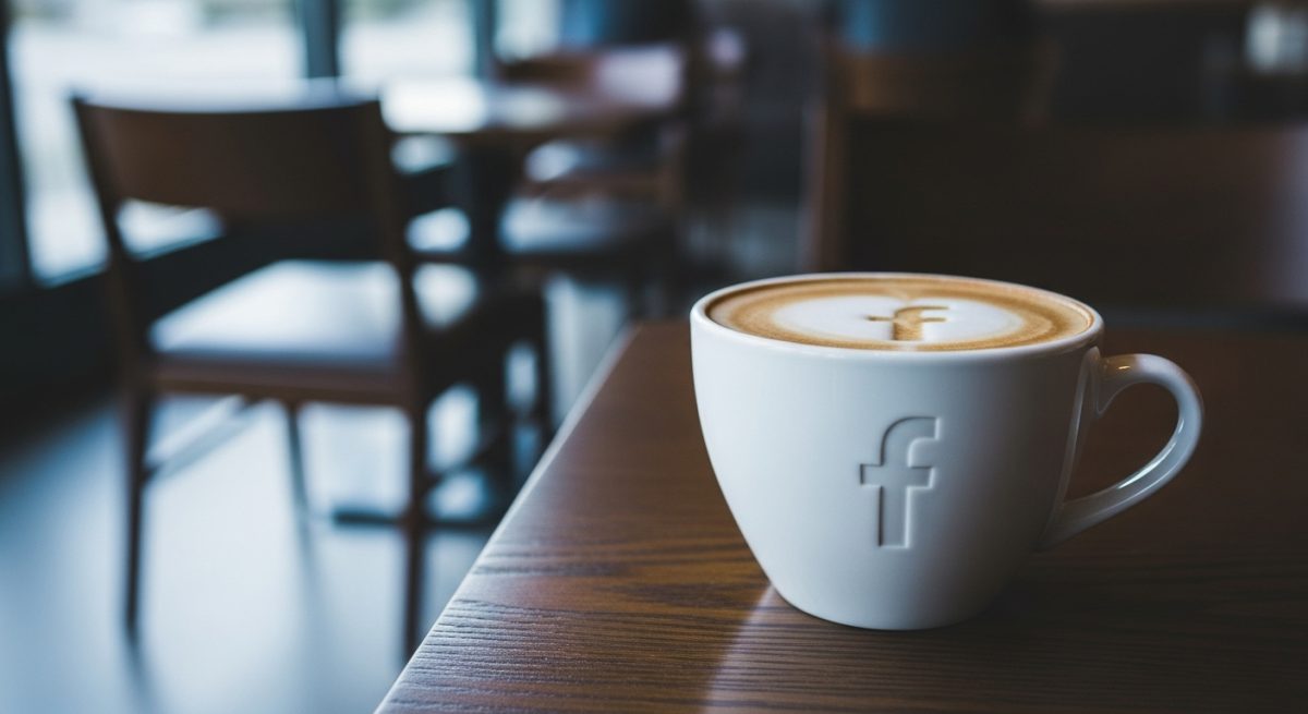 Taza café blanca con logo Facebook sobre mesa madera oscura