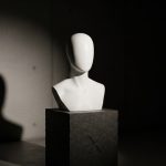 Busto de maniquí blanco mate con logo X en pedestal oscuro