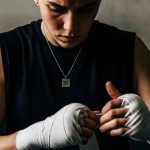Joven envolviendo manos con cinta de boxeo y colgante X