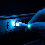 Mano sacando un cable de fibra óptica brillante de servidor con logo de Facebook