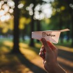 Mano soltando un avión de papel con logo de Instagram en parque sereno