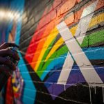 Mano sosteniendo spray pintando un logo X blanco en mural