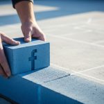 Manos colocando un ladrillo azul con logo de Facebook en obra