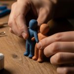 Manos de artista moldeando figurines de arcilla en mesa rústica