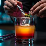 Manos de mixólogo agregando guarnición a un cóctel con logo TikTok