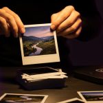 Manos hojeando fotografías Polaroid sobre escritorio con lámpara Instagram