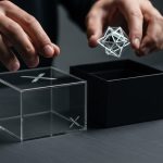 Manos sobre cajas modernas con logo X y objeto brillante