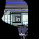 Silueta de persona en habitación oscura mirando oficina con logo de LinkedIn