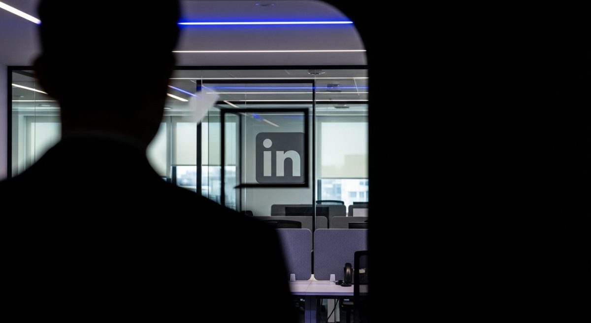 Silueta de persona en habitación oscura mirando oficina con logo de LinkedIn