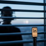 Silueta detrás de persianas venecianas con logo minimalista de LinkedIn